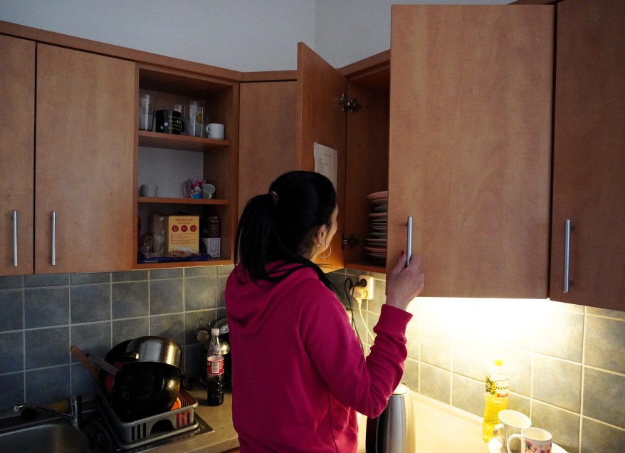 žena otvírá kuchyňskou skříňku nad sebou a vybírá si talíř